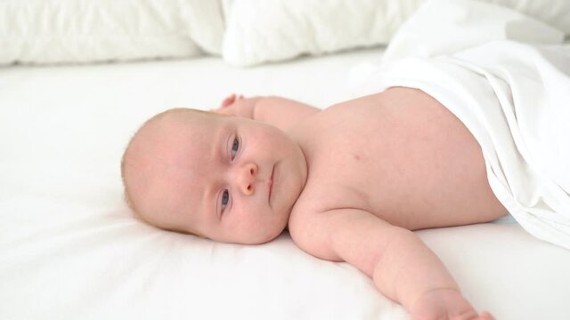 cute red-haired baby lies on a white bed.