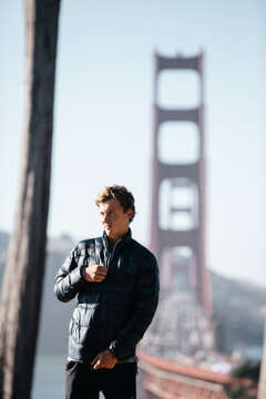 Young man fixing his down jacket beside the Golden Gate bridge in California