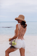 Young pretty caucasian tanned fit woman in knitted clothes and hat on beach  