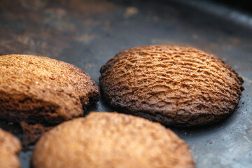 Burnt cookies. Burnt, burnt oatmeal cookies lie on a black baking sheet. Vertical photo