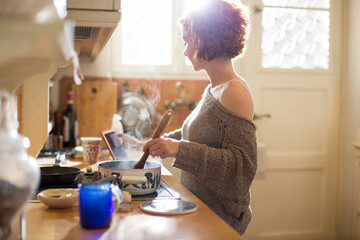 Young woman cooking while she is using a digital tablet