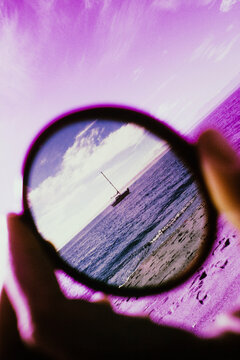Close up of hand holding corrective photography filter, sailboat in distance