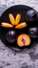 Plum whole and sliced on a black plate