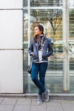 Young woman in blue leather jacket standing alone by the street waiting for friend
