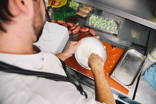 Over the shoulder view of a chef or cook preparing a meal by stirring the cream