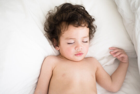 curly haired little boy sound asleep on white