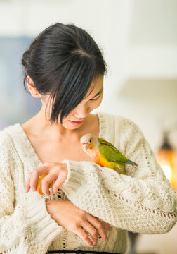 Attractive young Asian woman tenderly feeding a small pet parrot perched on her hand