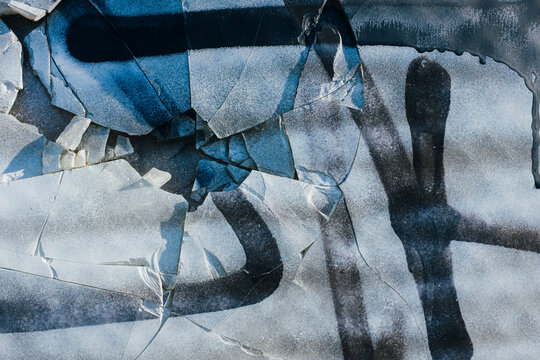 Spray painted graffiti on broken glass window of building exterior, close up
