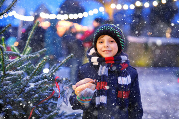 Little cute kid boy eating German sausage and drinking hot children punch on Christmas market. Happy child on traditional family market in Germany. Laughing boy in colorful winter clothes