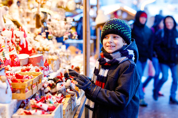 Little cute kid boy selecting decoration on Christmas market. Beautiful child shopping for toys and decorative ornaments stuff for tree. Xmas market in Germany.