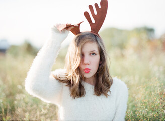 Silly teen girl in fuzzy white sweater wearing reindeer antlers