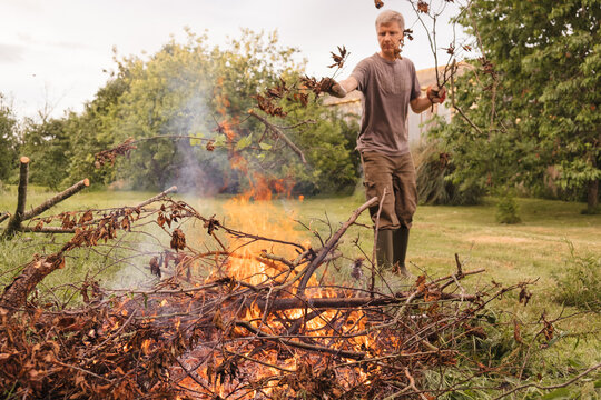 Man throwing branches onto garden bonfire