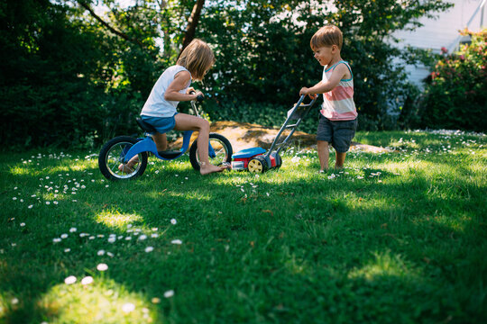 Little girl and boy playing together in backyard with bike and lawmower