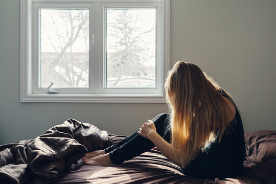 Blonde woman in a bedroom sitting on a bed with rumpled sheets.