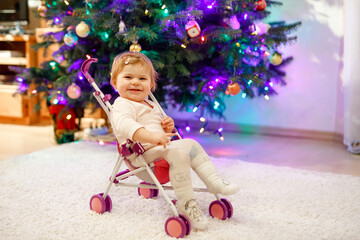 Cute adorable baby girl having fun with with doll carriage. Beautiful toddler child sitting in...