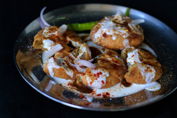 Indian chat kachori topped with curd and onions and laid on a black background