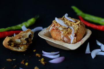 Indian chat kachori topped with curd and onions and laid on a black background