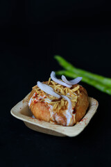 Indian chat kachori topped with curd and onions and laid on a black background