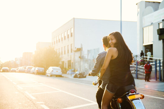 Couple riding into city sunset on motorcycle.