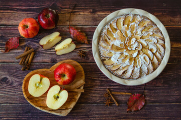 Homemade apple pie on a wooden table. The table is decorated with apples, leaves, cinnamon sticks and anise stars. Autumn atmosphere.