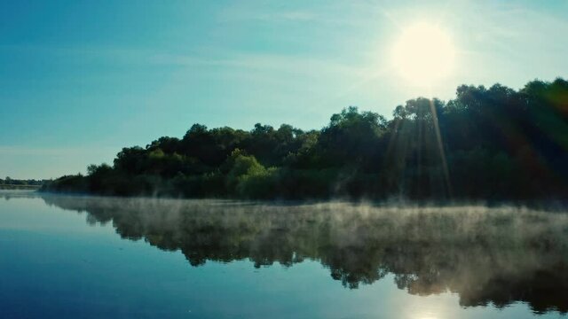 Drone flies close to water surface while morning evaporation. Beautiful morning landscape with a fog while sunrise. Aerial view of sunrise  above river Desna, Ukraine.  Water evaporation over the lake