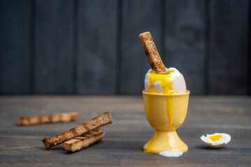 Soft boiled brown egg and toast bread in eggcup on wooden table background. Close up