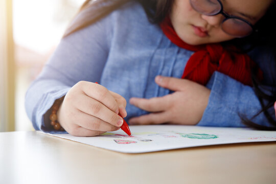 Girl with Down's syndrome drawing picture with crayon.