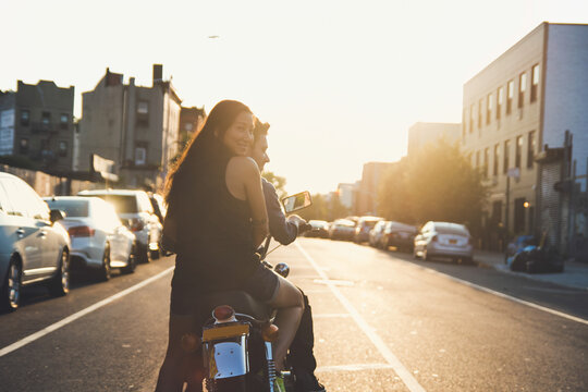 Couple riding into city sunset on motorcycle.