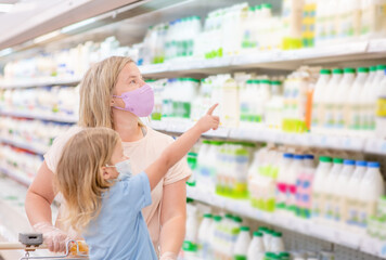 Mother and her little daughter wearing protective face mask shop a food at a supermarket during the coronavirus epidemic or flu outbreak