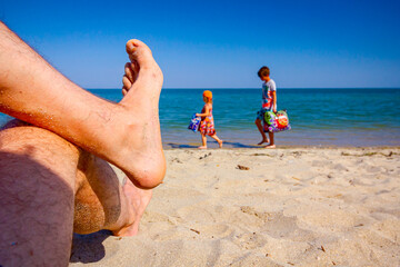 Man's crossed legs on the beach, relaxing by the sandy beach
