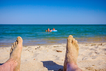 Fototapeta na wymiar Man's legs on the beach, relaxing by the sandy beach