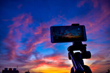 A mobile is placed on a tripod stand with a beautiful view on the sky behind. Reddish blue evening...