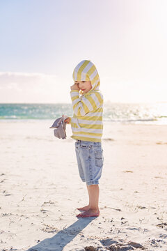 Small boy wiping sand from his eyes at the beach on a windy afternoon