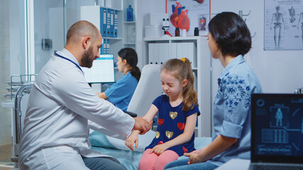 Doctor checking child injured arm and talking with mother. Healthcare practitioner physician...