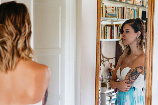 young female with tattoos looking in mirror wearing dress