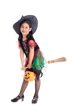 Full length of little asian girl in witch costume with make up riding on broom and smiles over white background. Child Halloween costume concept.