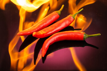 red hot long chili peppers burning on fire on a red dark background
