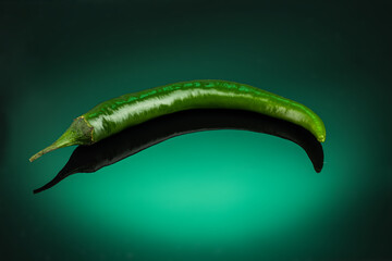 green hot chili peppers on dark green background with reflection