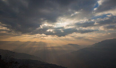 Sun breaking through veil of clouds in himalayan hills.
