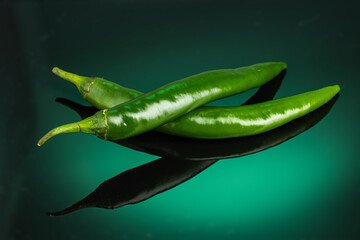 green hot chili peppers on dark green background with reflection