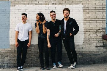 diverse group of four friends who are in a band stand against wall for promo photos