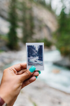 Woman holding a polaroid up infront of a river in nature