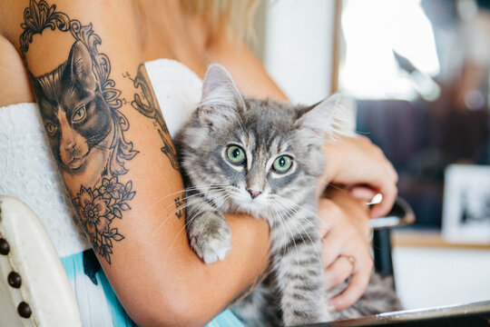 young woman with tattoos holds cat in home while sitting in chair