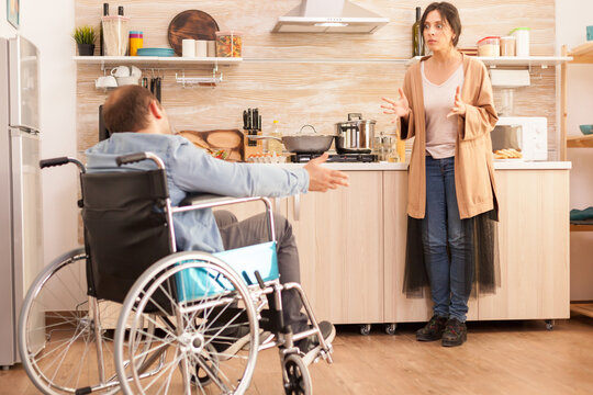Wife looking angry at disabled man in wheelchair during an argument about their relationship in kitchen. Disabled paralyzed handicapped man with walking disability integrating after an accident.
