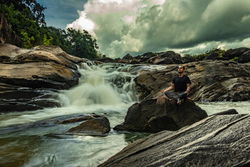 man meditating at rock with the beautiful waterfall stream at evening