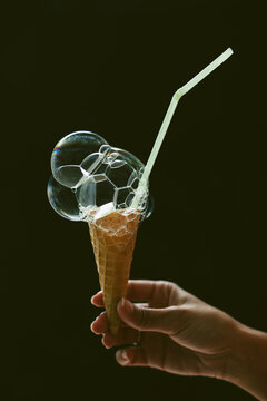 Hand holding a soap bubble ice cream on a black background.