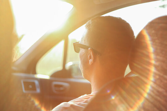 Young man sitting in a car. From teh back, contra light.