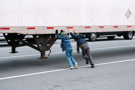 Two kids trying hard to push a parked trailer truck.