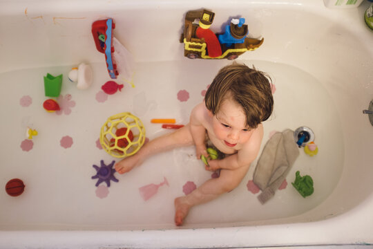 A young boy in a tub surrounded by bath toys.