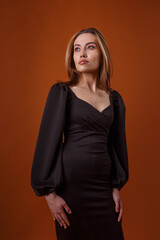 Fototapeta premium charming elegant fashion model wearing black dress with deep neckline posing on orange background. asian skinny young woman in sexy evening gown. beautiful sensual glamorous lady poses in studio
